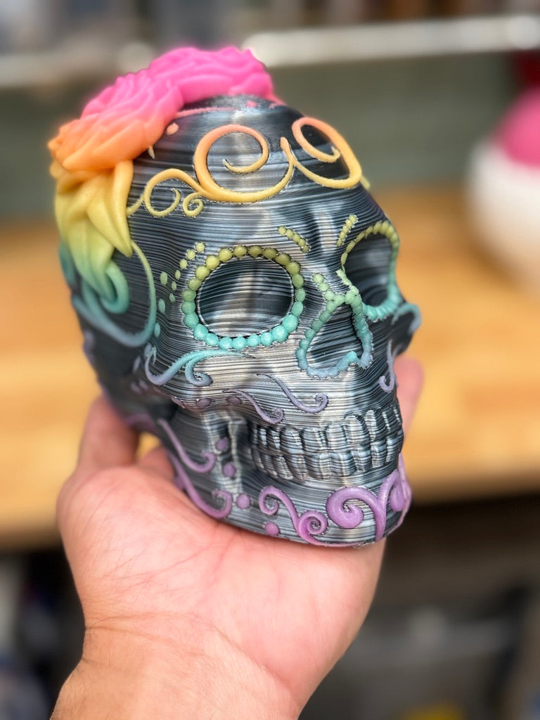 Día de los Muertos-inspired 3D printed skull with rainbow floral details, held in a hand